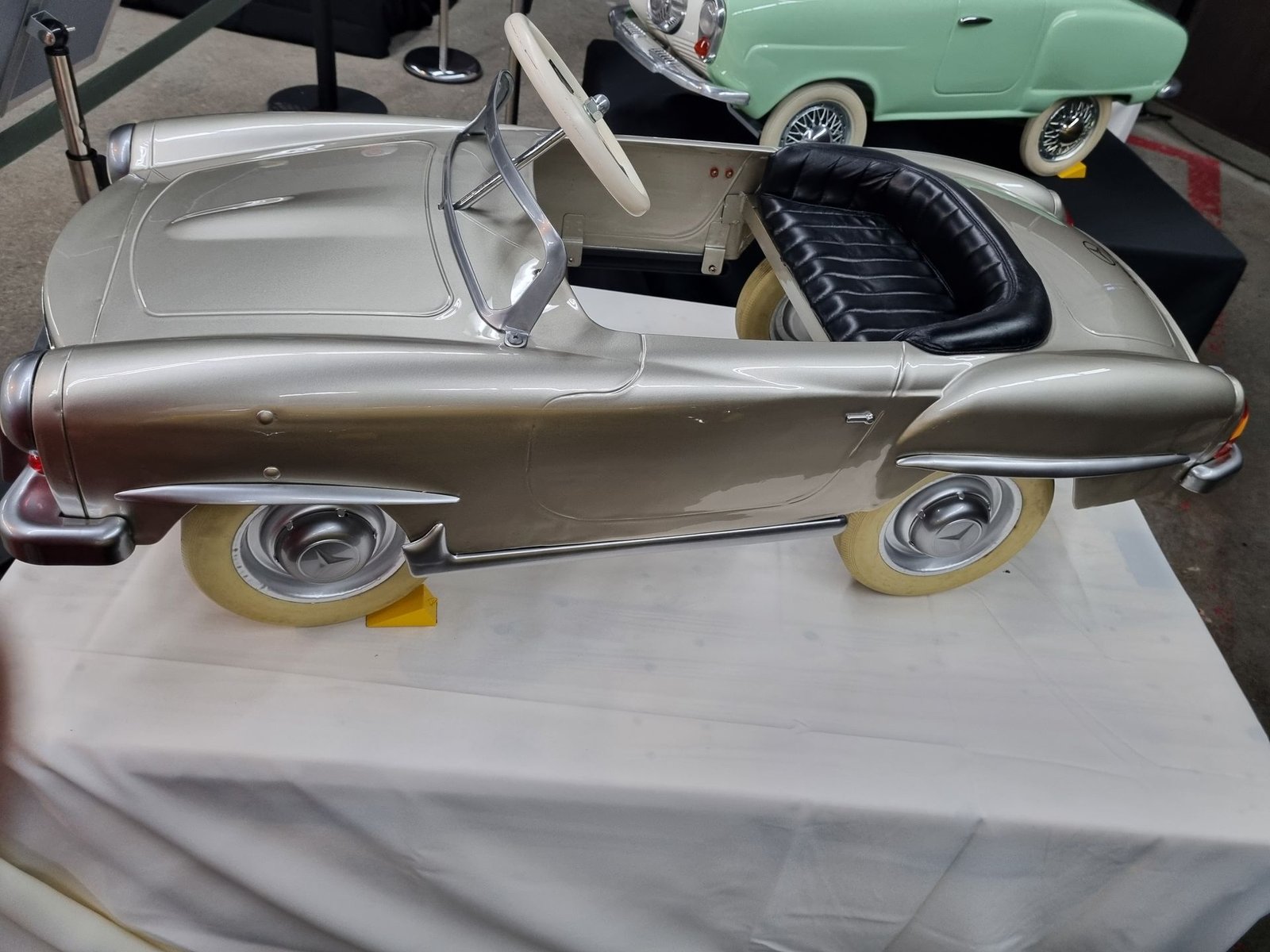 Auf einem weißen Tisch steht ein silbernes Tretauto.